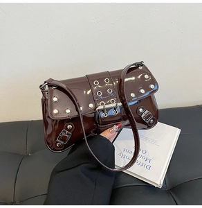 Detail of dark brown patent leather underarm bag with silver rivets and buckle straps