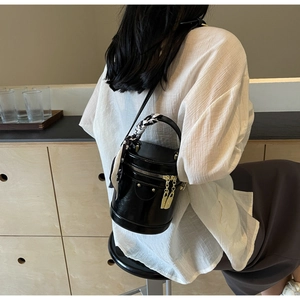 Détail du sac cylindrique noir brillant avec fermeture dorée et poignée ornée d'un foulard