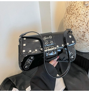 Close-up of black patent leather underarm bag featuring silver rivets and metal buckle detail