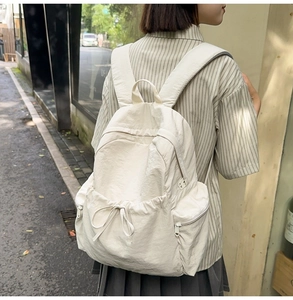 Outdoor shot of a cream white nylon backpack with drawstring front pocket and side zippers
