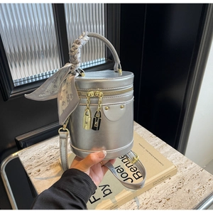 Close-up of silver cylinder handbag with decorative silk scarf and golden lock zipper detail