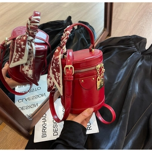 Détail du sac cylindrique rouge en cuir huilé avec foulard en soie et ornement de cadenas