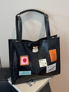 Glänzende schwarze Tragetasche mit süßen Patches und Cartoons auf einem Magazin