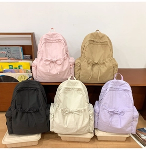 Detail view of nylon backpacks in multiple colors featuring decorative drawstring bows