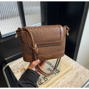 Détail d'un sac seau en cuir tressé marron foncé avec logo doré et bandoulière fine