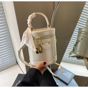 Detail of cream cylindrical bucket bag with gold chain zipper and silk scarf handle decor