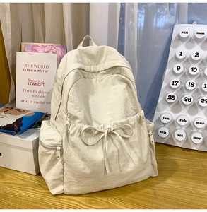 Close-up of beige nylon backpack featuring elegant bow drawstring and side zipper pockets