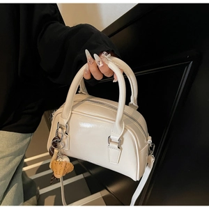 Detailed side view of a creamy white glossy patent leather bowling bag with a cute bear charm