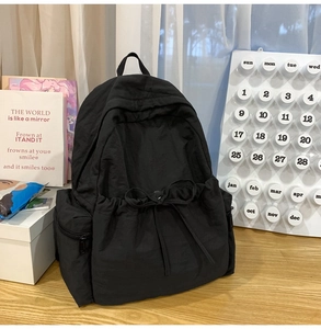 Detailed view of black nylon backpack with decorative drawstring bow and side zipper pocket