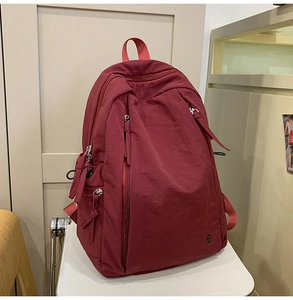 Detail of burgundy nylon backpack texture with side pockets and zipper pulls on a stool