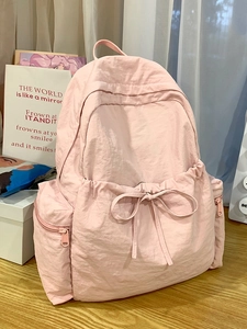 Pink ballet-style nylon backpack with ribbon bow detail on a minimalist wood desk