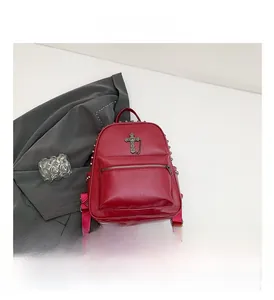 Detail of dark red leather backpack featuring cross pendant, metal rivets and fabric strap