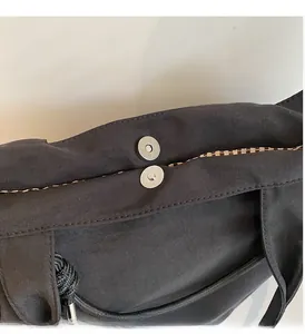 Detail view of the silver magnetic clasp and beige plaid lining on the black tote bag