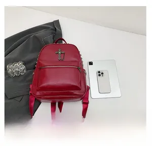 Detail shot of a red leather backpack featuring metal cross charms and side rivet studs