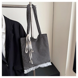Detail of checkered tote bag with white lace trim and ribbon on a metal rack