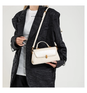 Detail einer cremefarbenen Ledertasche mit goldener Schnalle und strukturiertem Blazer-Hintergrund
