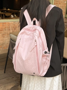 Pink lightweight nylon backpack with bear logo for women shown in outdoor cafe setting
