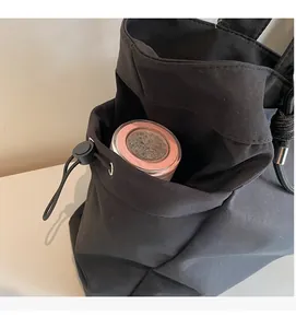 Detail of black nylon tote bag side pocket with drawstring holding a water bottle