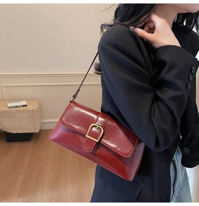 Détail d'un sac baguette bordeaux foncé en cuir ciré porté avec un blazer élégant