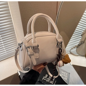 Detail view of cream Boston handbag with silver hardware and baseball charm accessory