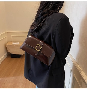 Sac baguette en cuir verni marron foncé avec boucle dorée porté à l'épaule par un mannequin