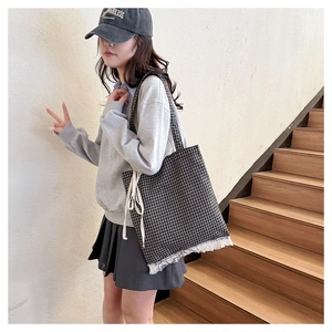 Detail of checkered canvas tote bag featuring white lace trim and bow on the side