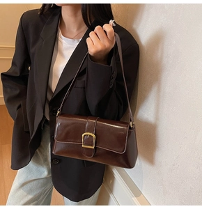 Détail d'un sac baguette marron foncé avec une boucle dorée sur la bandoulière réglable