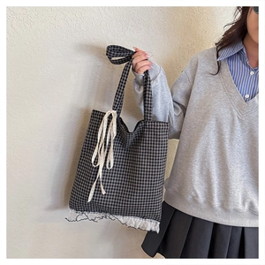 Detail of checkered tote bag featuring white lace ruffles and a sweet ribbon bow