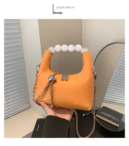 Détail du sac à main orange avec de grandes perles sur l'anse et une chaîne argentée