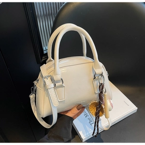 Close-up of a white bowling-style bag with silver metal buckles and baseball charm accessory
