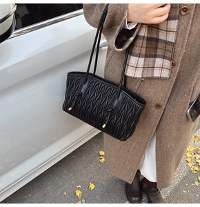 Chic black pleated shoulder bag styled with a brown wool coat in an autumn street setting