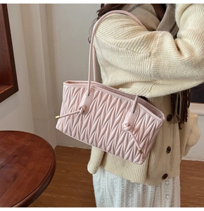 Side view of soft pink pleated shoulder bag worn by model in a cozy interior setting