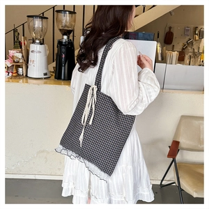 Detailed view of checkered canvas tote bag with lace trim and bow in a cafe setting