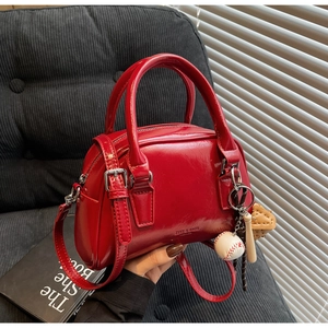 Close-up of a red glossy bowling bag featuring a vintage baseball charm and detachable strap