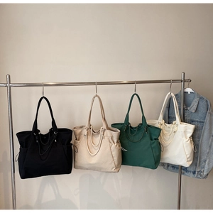 Detail showing four solid color tote bags in black, beige, green, and cream on a rack