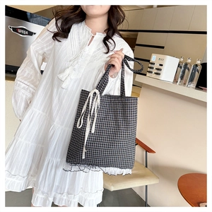 Detail of checkered tote bag with white lace trim carried by a model in a cafe setting