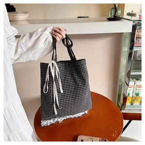 Detailed view of black and white gingham tote bag with lace trim and bow on wooden table