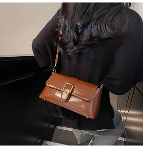 Détail du sac baguette marron verni avec boucle dorée et bandoulière sur un mannequin