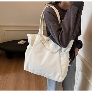 Detail view of large cream canvas tote bag with side pocket shown on shoulder