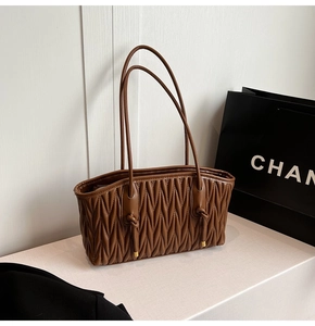 Detail of a brown pleated quilted tote bag featuring slim shoulder straps and knot decor