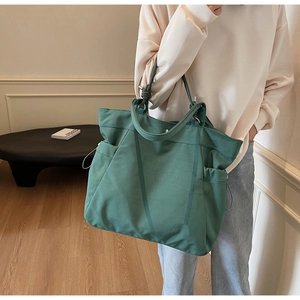 Detail showing side drawstring pocket and spacious canvas texture of the green tote bag