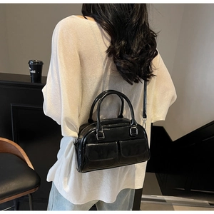 Close-up of a black glossy oil wax leather Boston bag featuring two front flap pockets