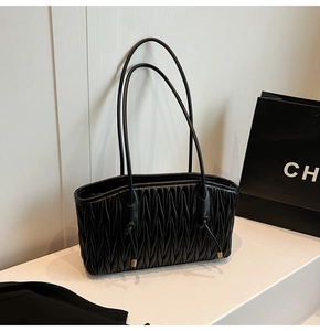 Close-up of the matelassé pleated texture and dual shoulder straps on a black tote bag