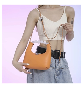 Detail of orange moon-shaped leather handbag with pearl handle and metal chain strap