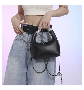 Détail d'un sac à main noir avec poignée perlée et bandoulière chaîne sur un modèle