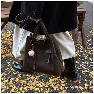 Borsa a secchiello marrone scuro con ciondolo a pompon su strada con foglie di ginkgo
