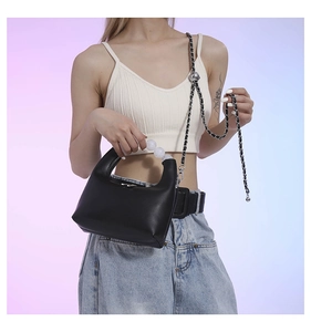 Detail of black crescent handbag featuring pearl handle and woven chain strap on model