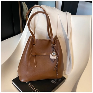 Dettaglio di una borsa a secchiello in pelle marrone con nappe e un ciondolo unico