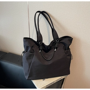 Close-up of black tote bag featuring drawstring side pockets and durable metal rings