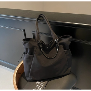 Detail of black nylon tote bag featuring side drawstring pocket and durable shoulder straps